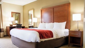 A hotel room with a large bed, two bedside tables, a wooden headboard, and two wall-mounted lamps.