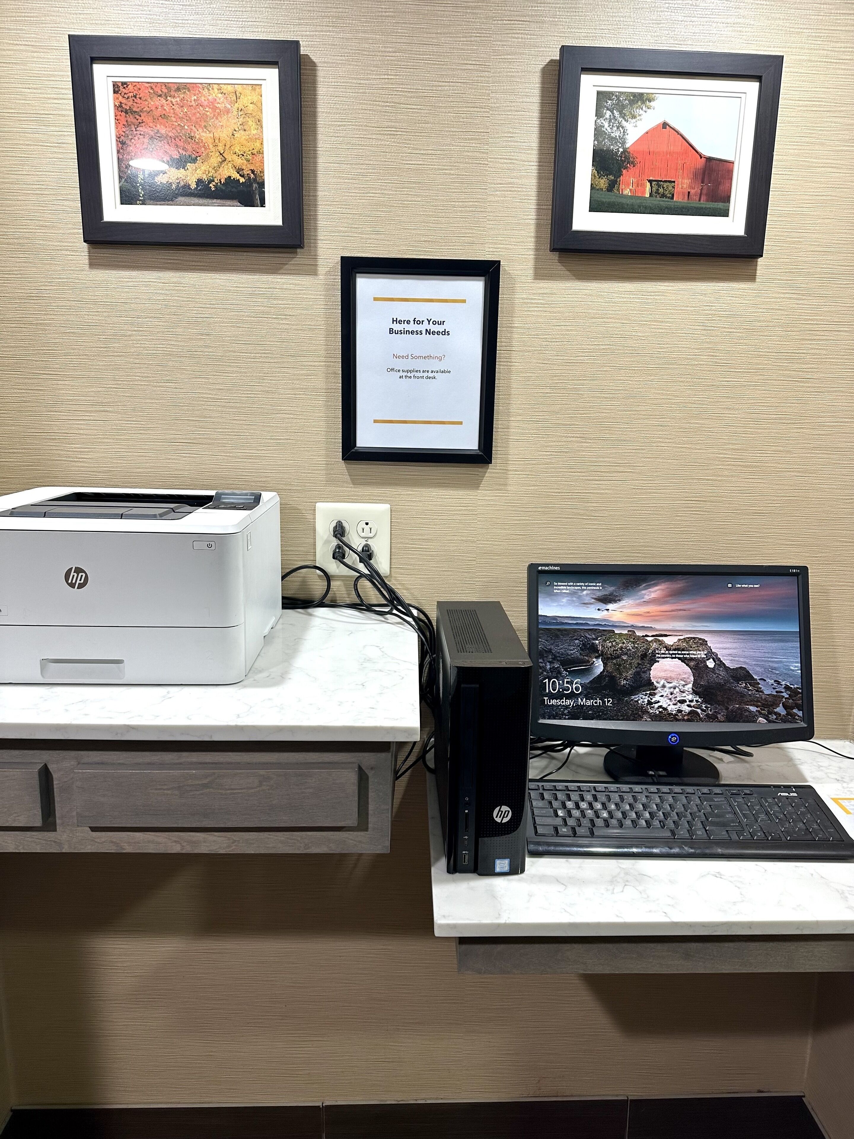 Un escritorio con una impresora HP, una computadora de escritorio y un cartel enmarcado en la pared.