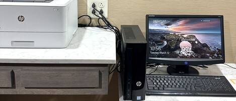 Un escritorio con una impresora HP, una computadora de escritorio y un cartel enmarcado en la pared.