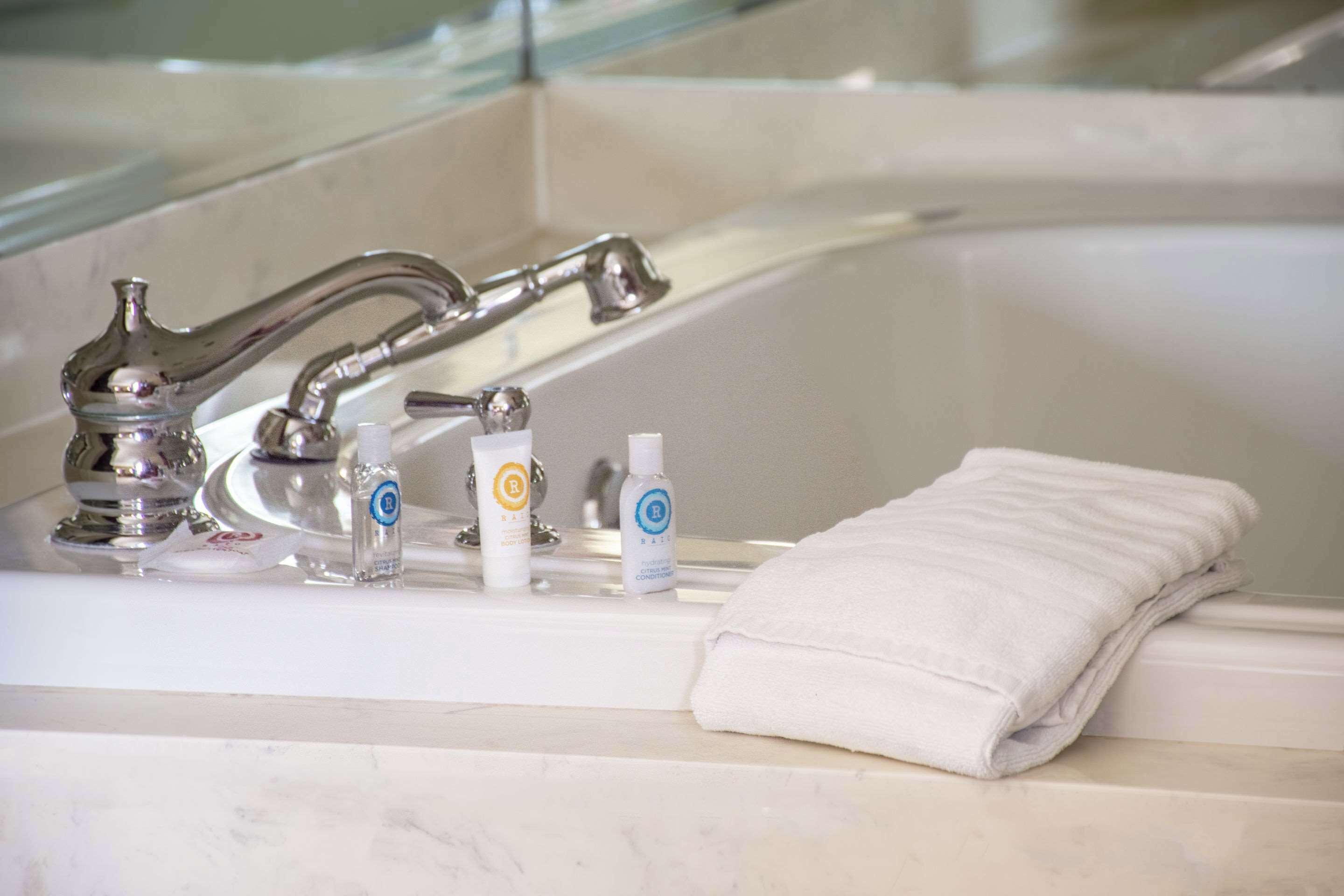Un baño con bañera, lavamanos con grifo moderno y artículos de tocador, incluyendo una botella de loción y una pastilla de jabón.