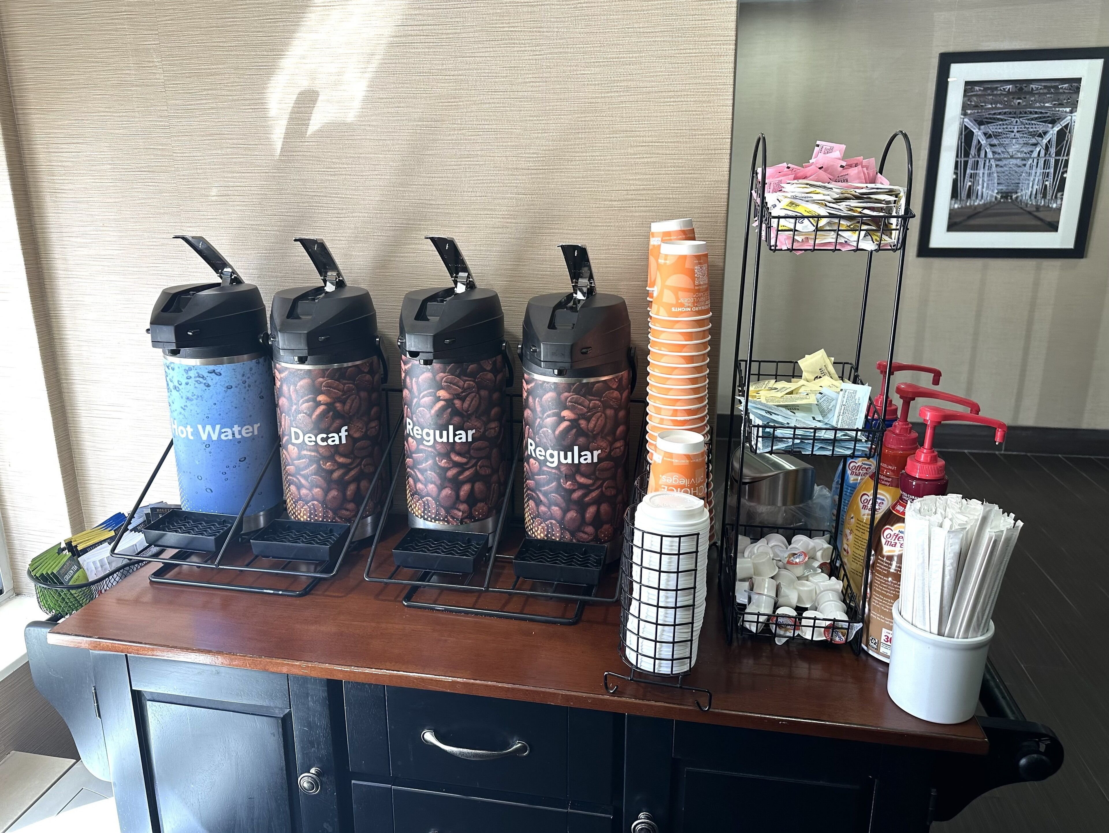 A coffee station with decaf, regular, and hot water dispensers, a coffee machine, and various coffee-related items.