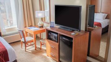 Habitació d'hotel amb escriptori de fusta, televisió, microones, nevera, llit i finestra amb cortines.