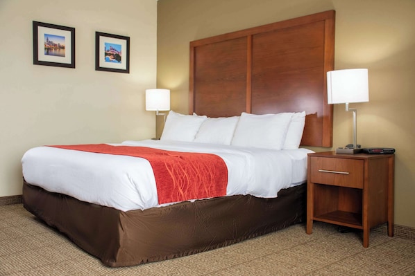 Cama bem arrumada com roupa de cama branca e vermelha, duas luminárias de cabeceira e uma mesinha de cabeceira de madeira com um controle remoto.