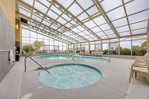 An indoor swimming pool with a glass ceiling, surrounded by lounge chairs and a view of the outdoors.