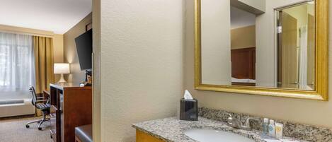 A hotel room with a desk, chair, and a large mirror above a granite countertop sink.