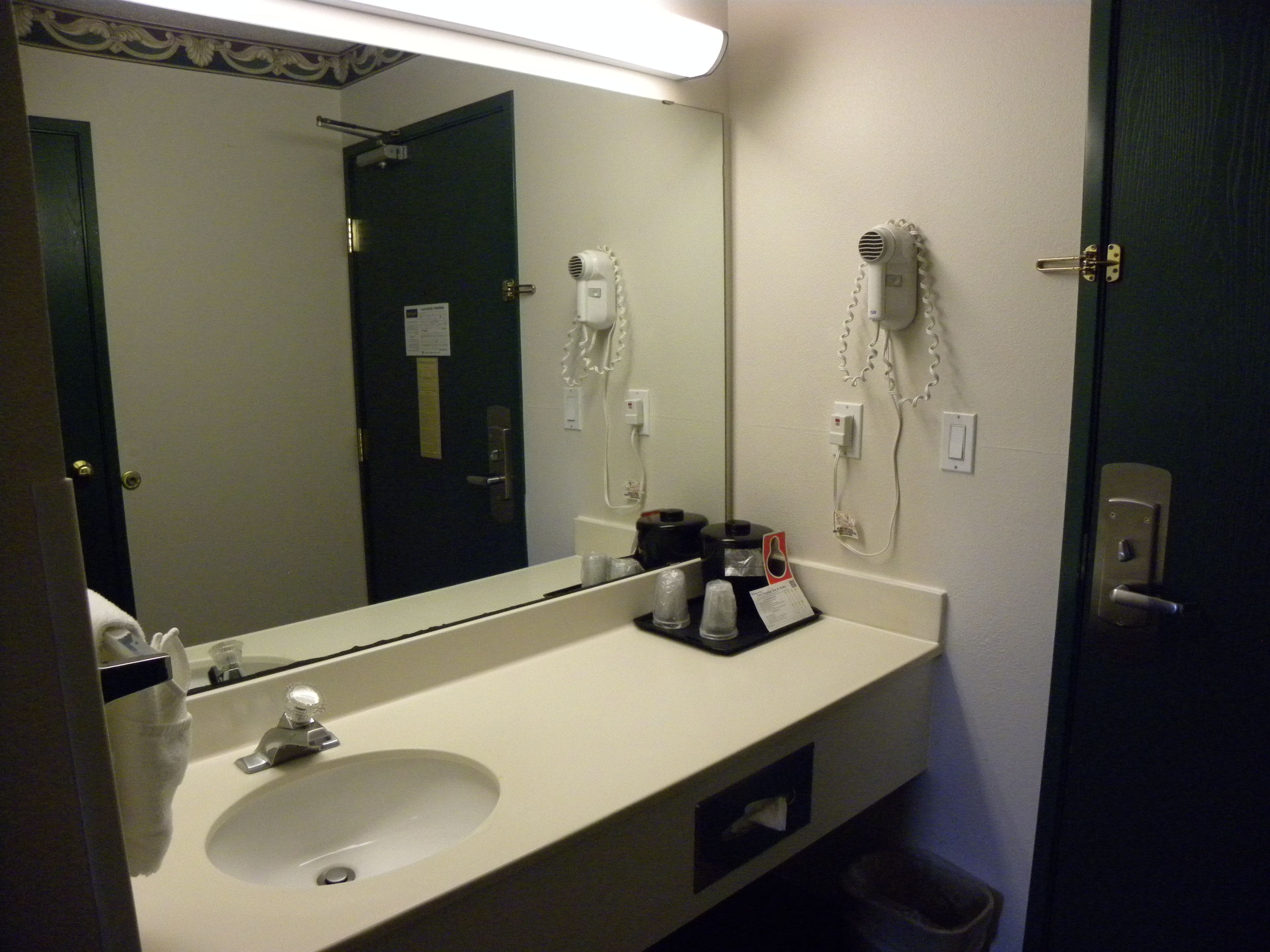 A hotel bathroom with a sink, mirror, hairdryer, and a trash bin.