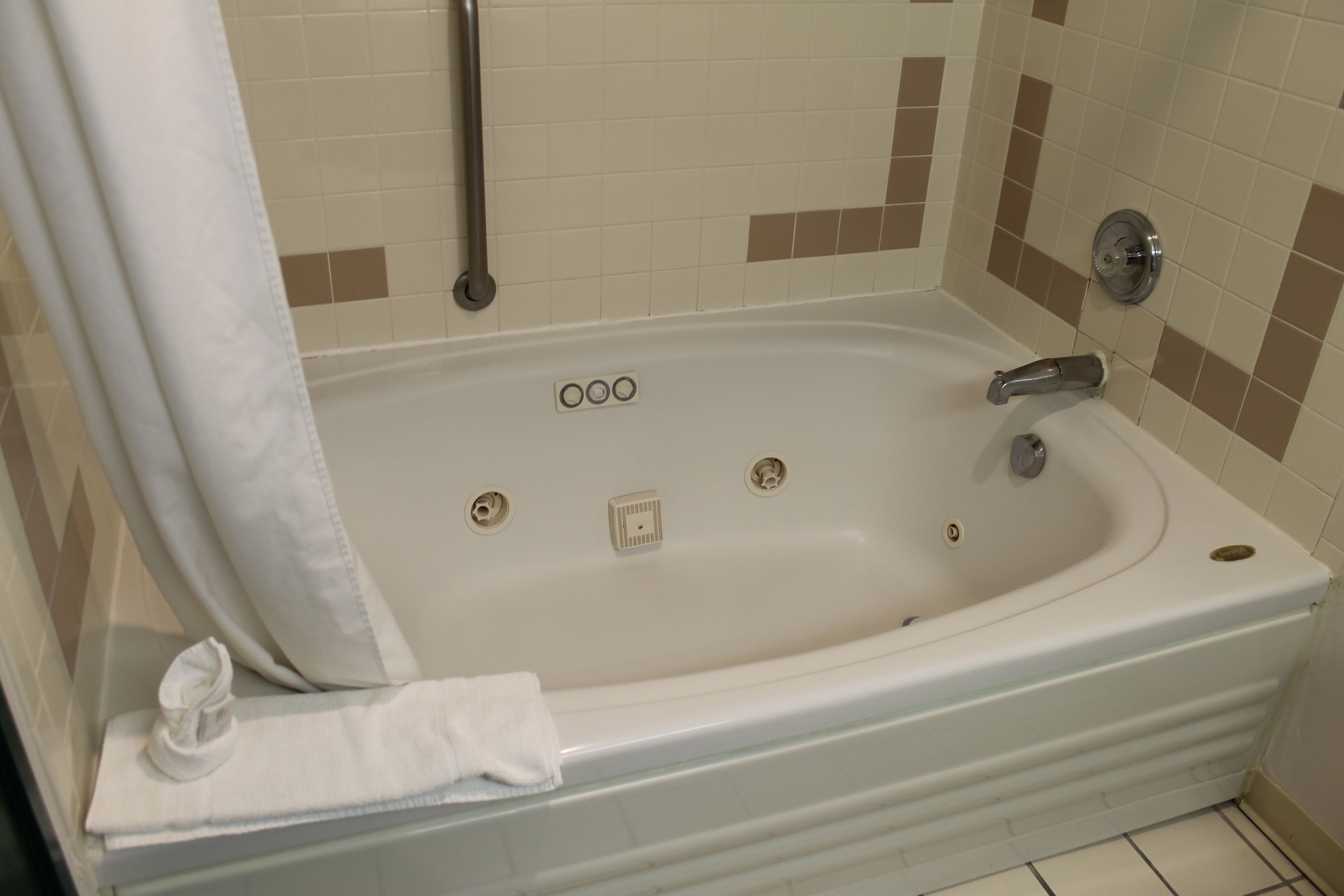 A bathroom with a white bathtub, a handrail, and a towel on the floor.