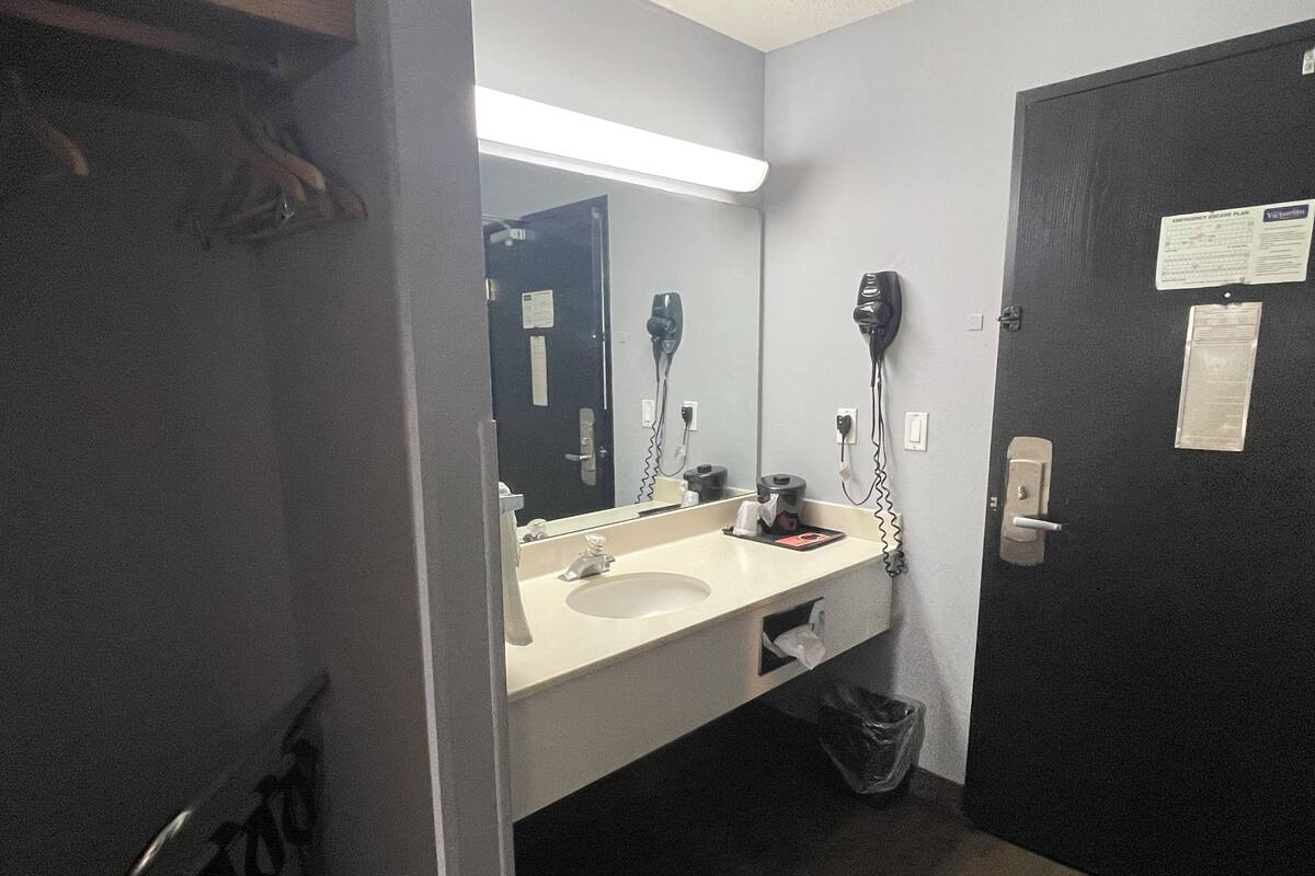 A bathroom with a sink, mirror, hair dryer, and a trash bin.