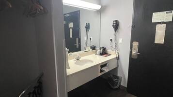 A bathroom with a sink, mirror, hair dryer, and a trash bin.