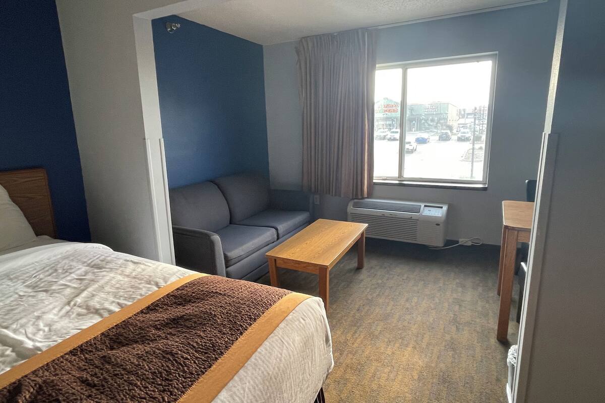A hotel room with a bed, a sofa, a small table, and a window with a view of the street.