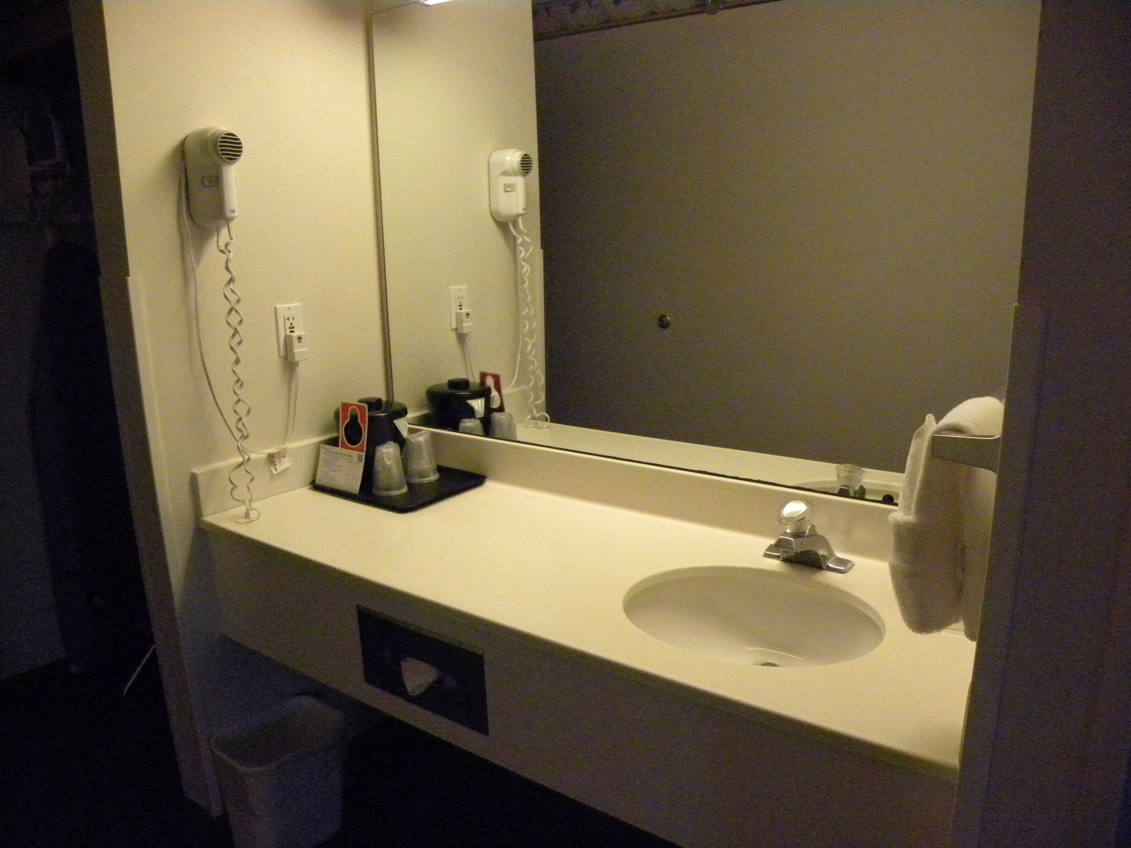 A bathroom with a white sink, a mirror, a hairdryer, and a towel rack.