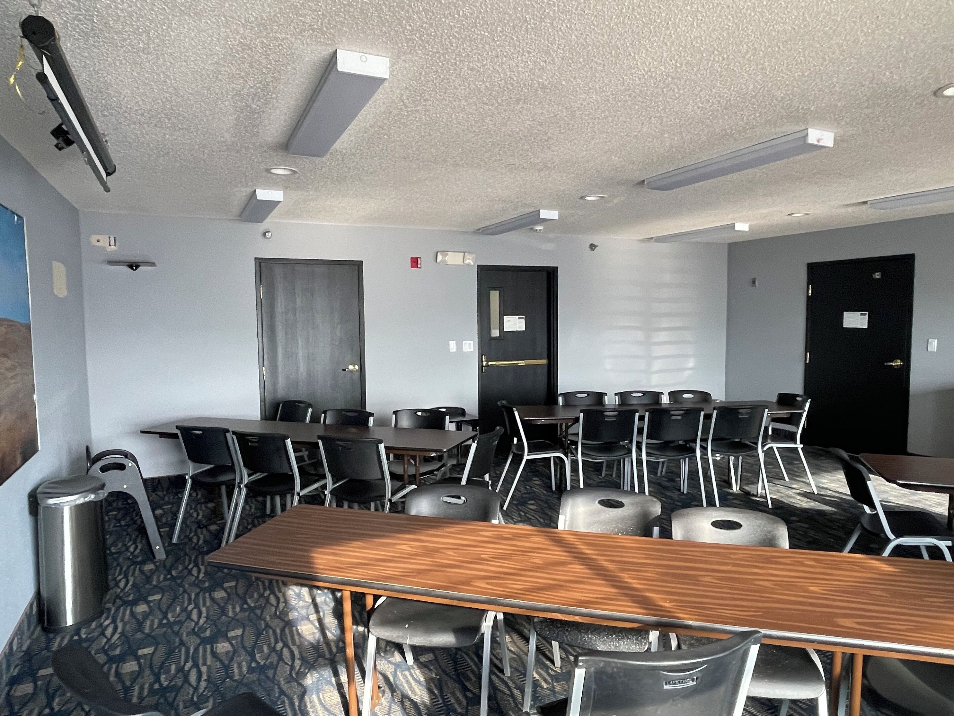 A conference room with multiple tables and chairs, ceiling lights, and doors.