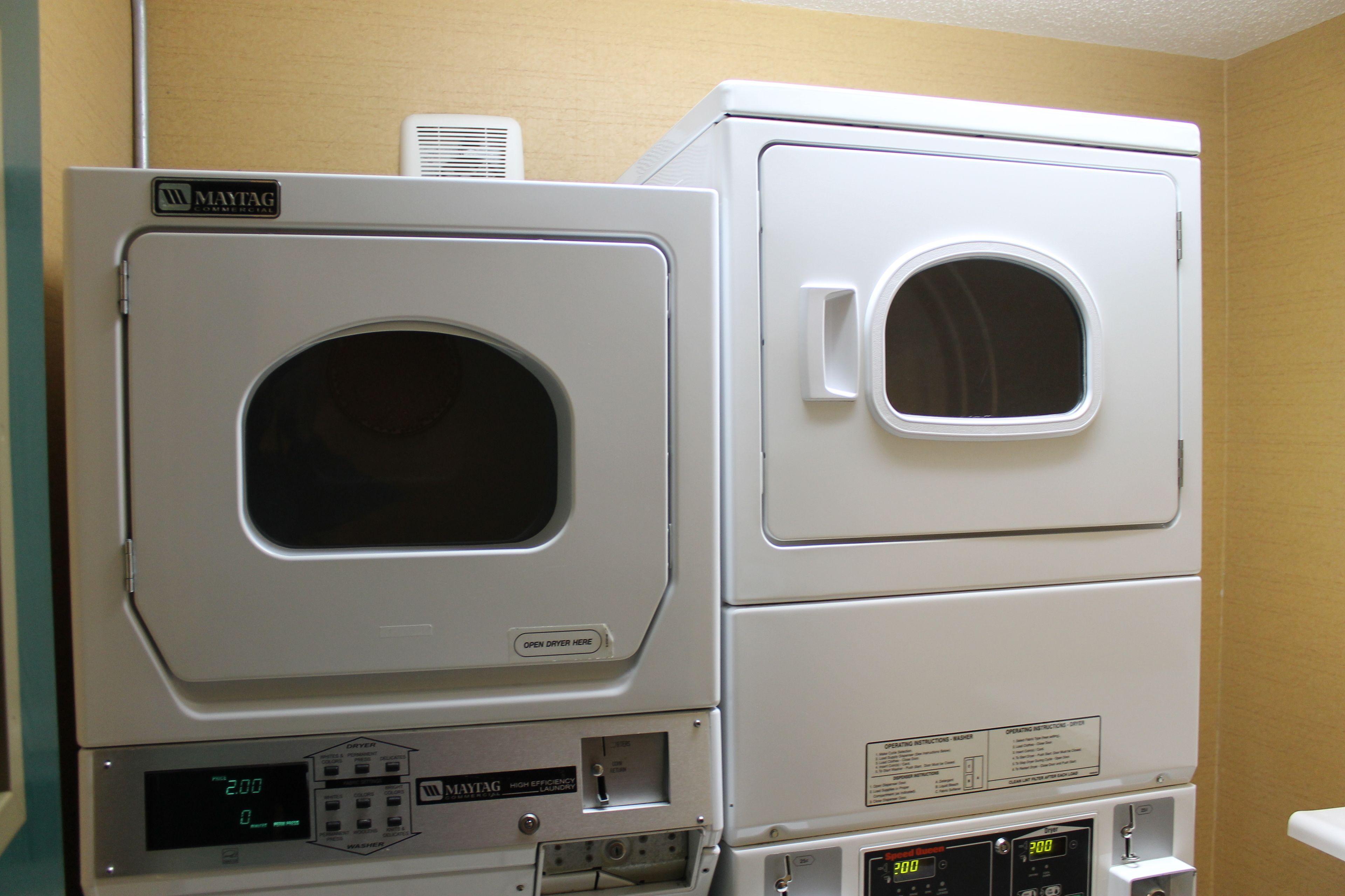 Een gestapelde wasmachine en droger met bedieningspanelen en een ventilatieopening.