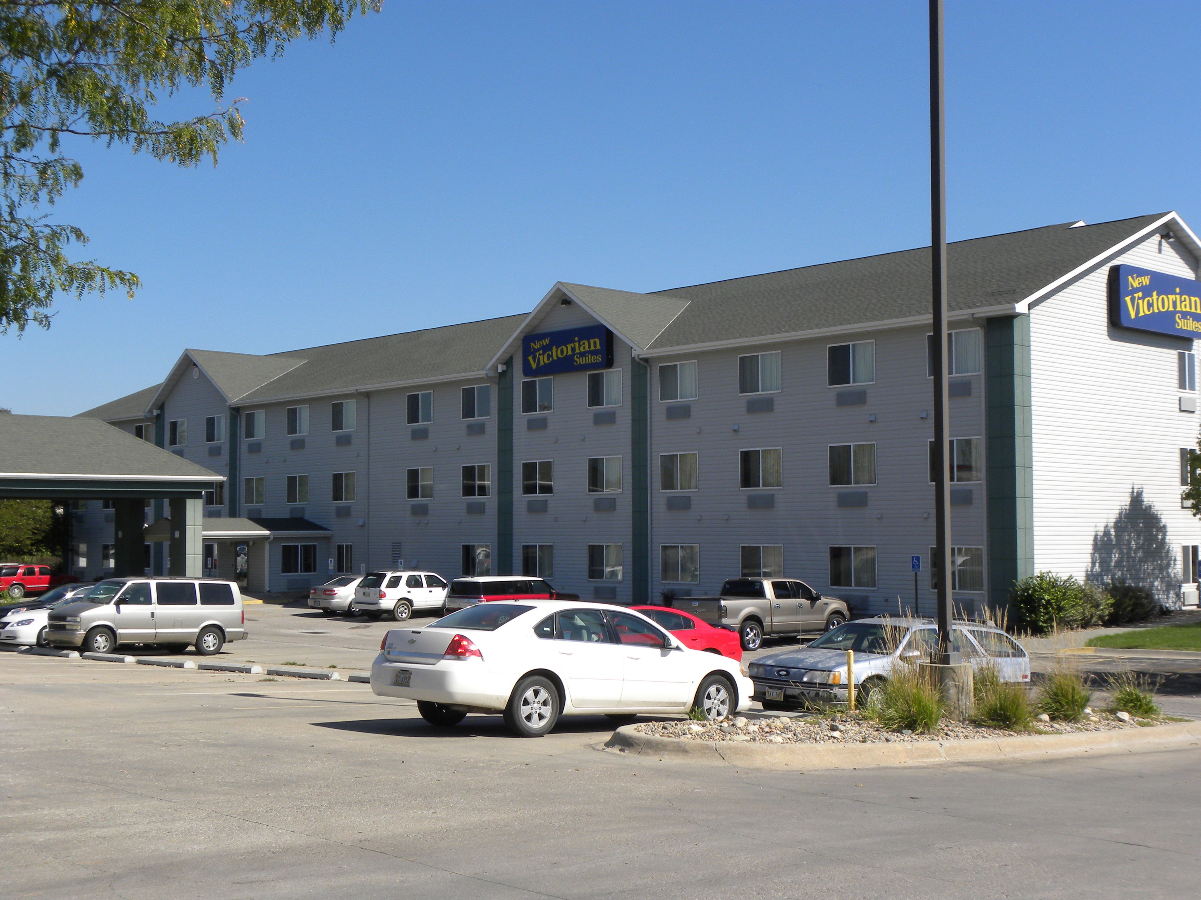 A hotel with multiple floors, a parking lot with several cars, and a sign indicating it is a new establishment.