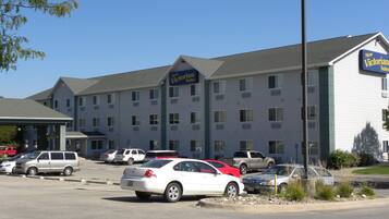 A hotel with multiple floors, a parking lot with several cars, and a sign indicating it is a new establishment.