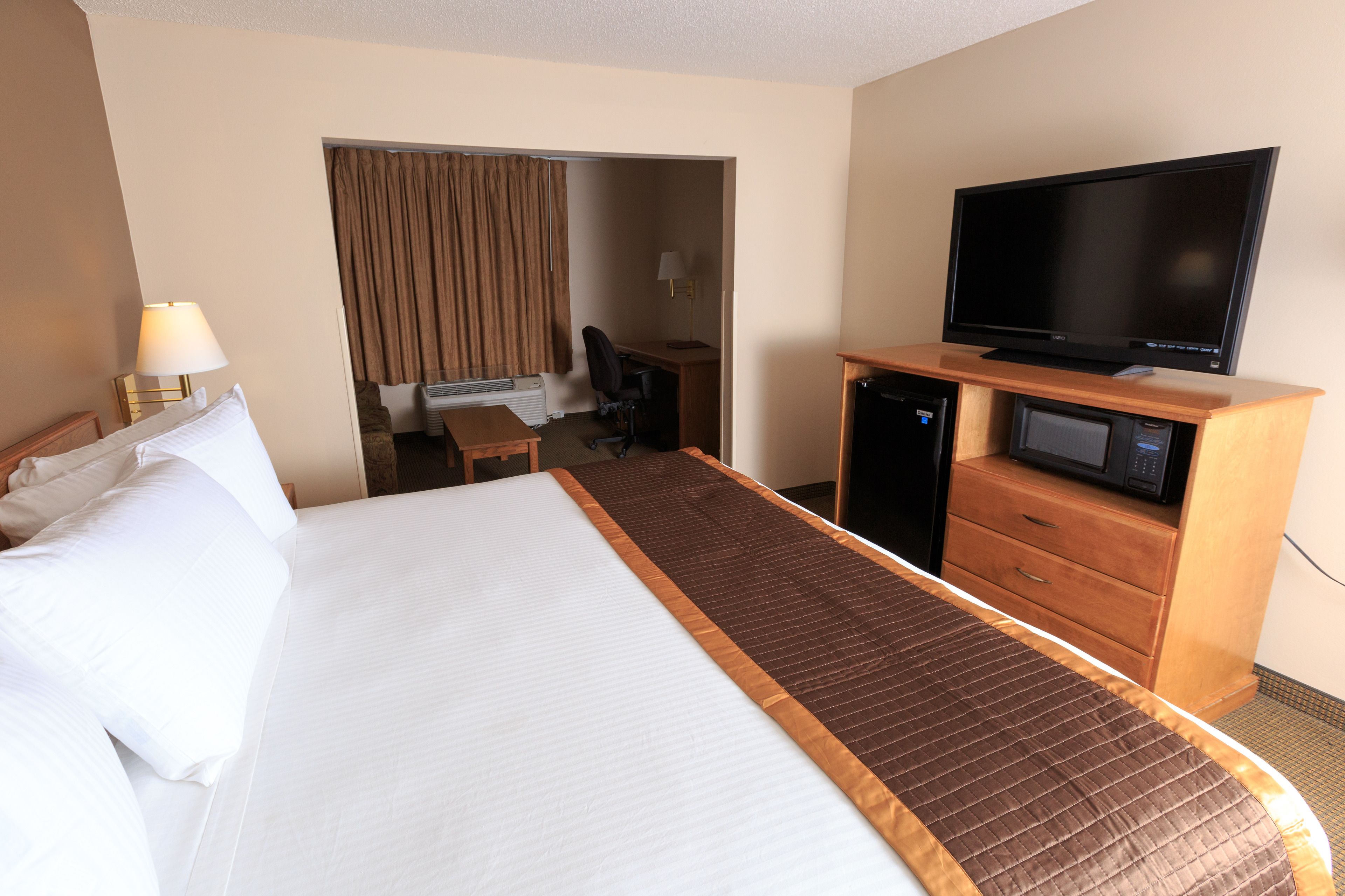 Ein Hotelzimmer mit einem großen Bett, einem Fernseher, einer Mikrowelle und einem Schreibtisch mit Stuhl.
