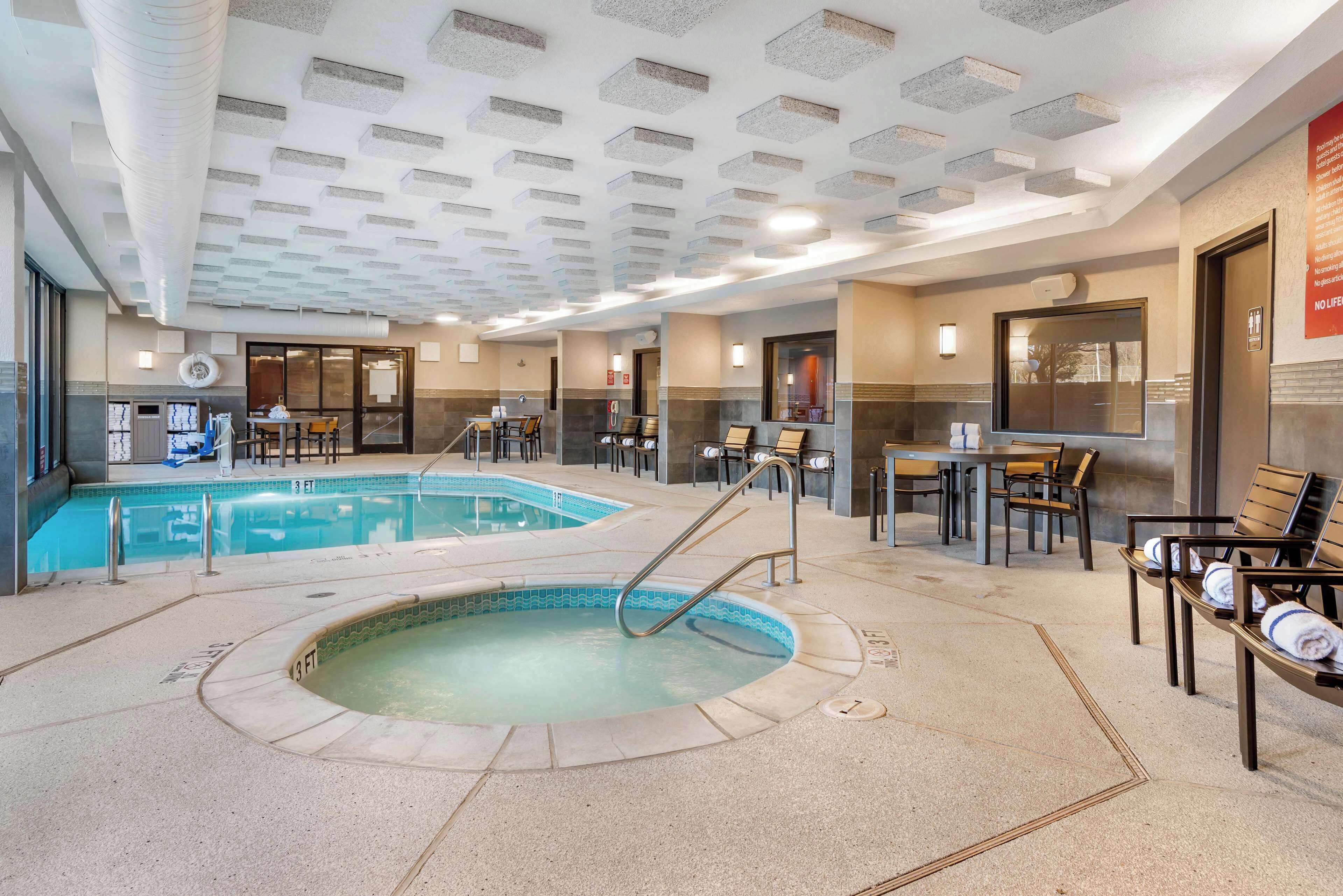 An indoor swimming pool with a hot tub, seating areas, and a ceiling with recessed lighting.
