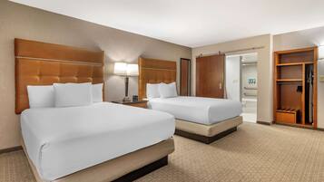 A hotel room with two beds, a nightstand, a lamp, a closet, and a bathroom visible through an open door.