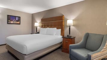 A hotel room with a large bed, two bedside lamps, a chair, and a framed picture on the wall.