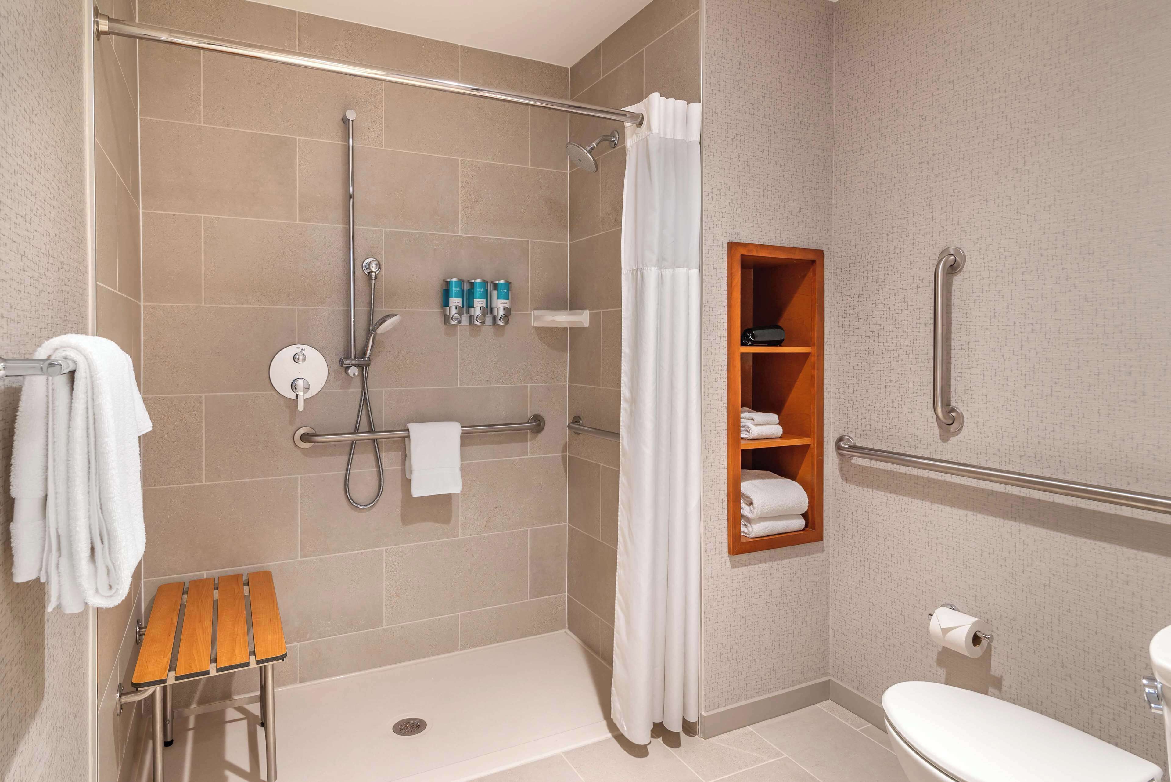 Un baño moderno con ducha, inodoro y un pequeño banco de madera.