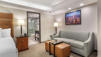 A hotel room with a bed, a grey sofa, a small table, and a cabinet.
