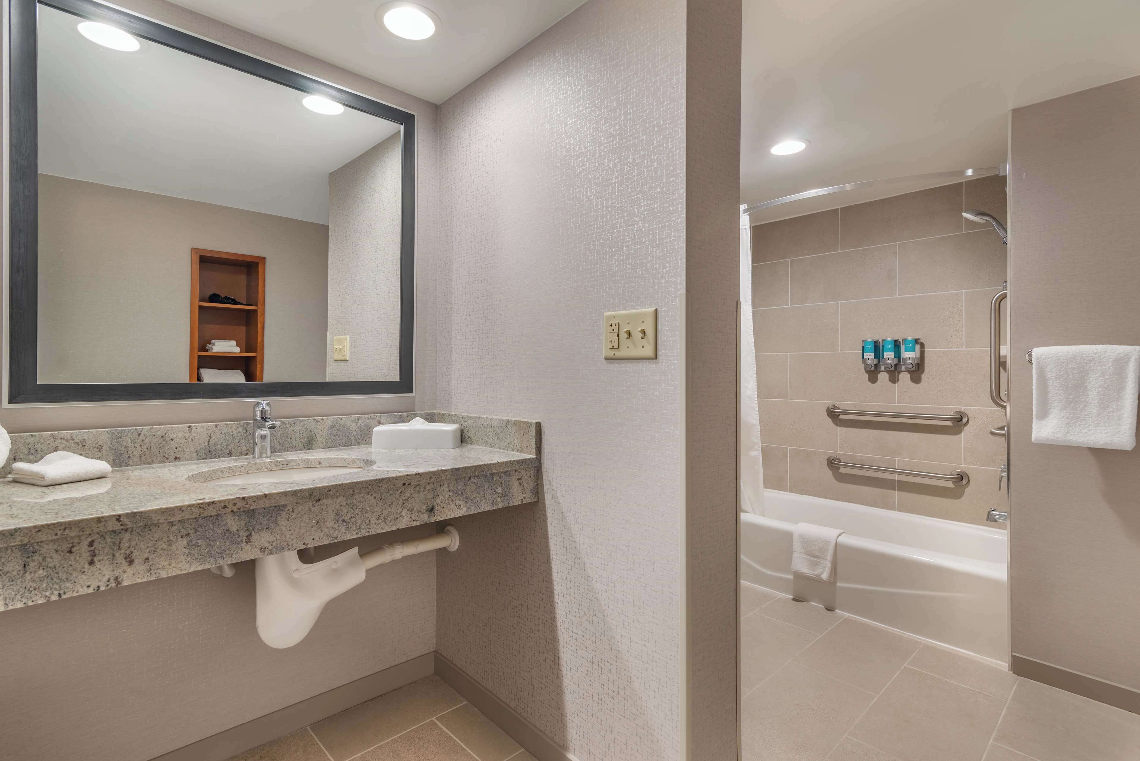 Un baño moderno con lavamanos de granito, un espejo grande, un perchero y una ducha a ras de suelo con bañera.
