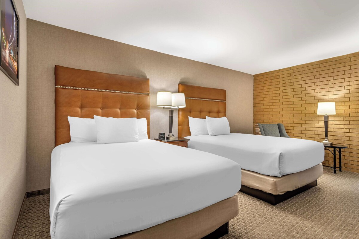 A hotel room with two beds, a brick-patterned wall, and a small table with a lamp.