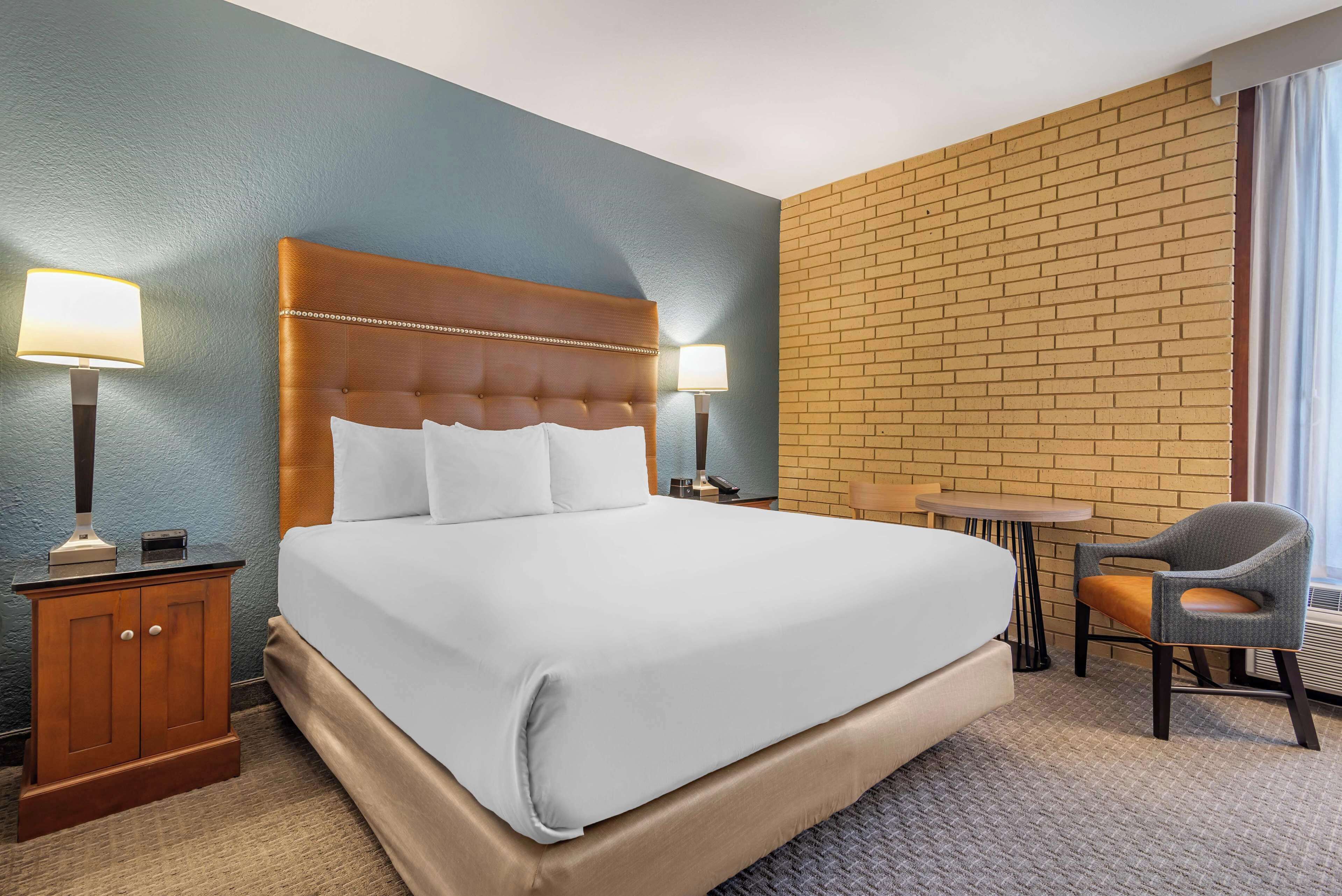 Una habitación de hotel con una cama grande, dos mesitas de noche, una silla y una pequeña mesa.