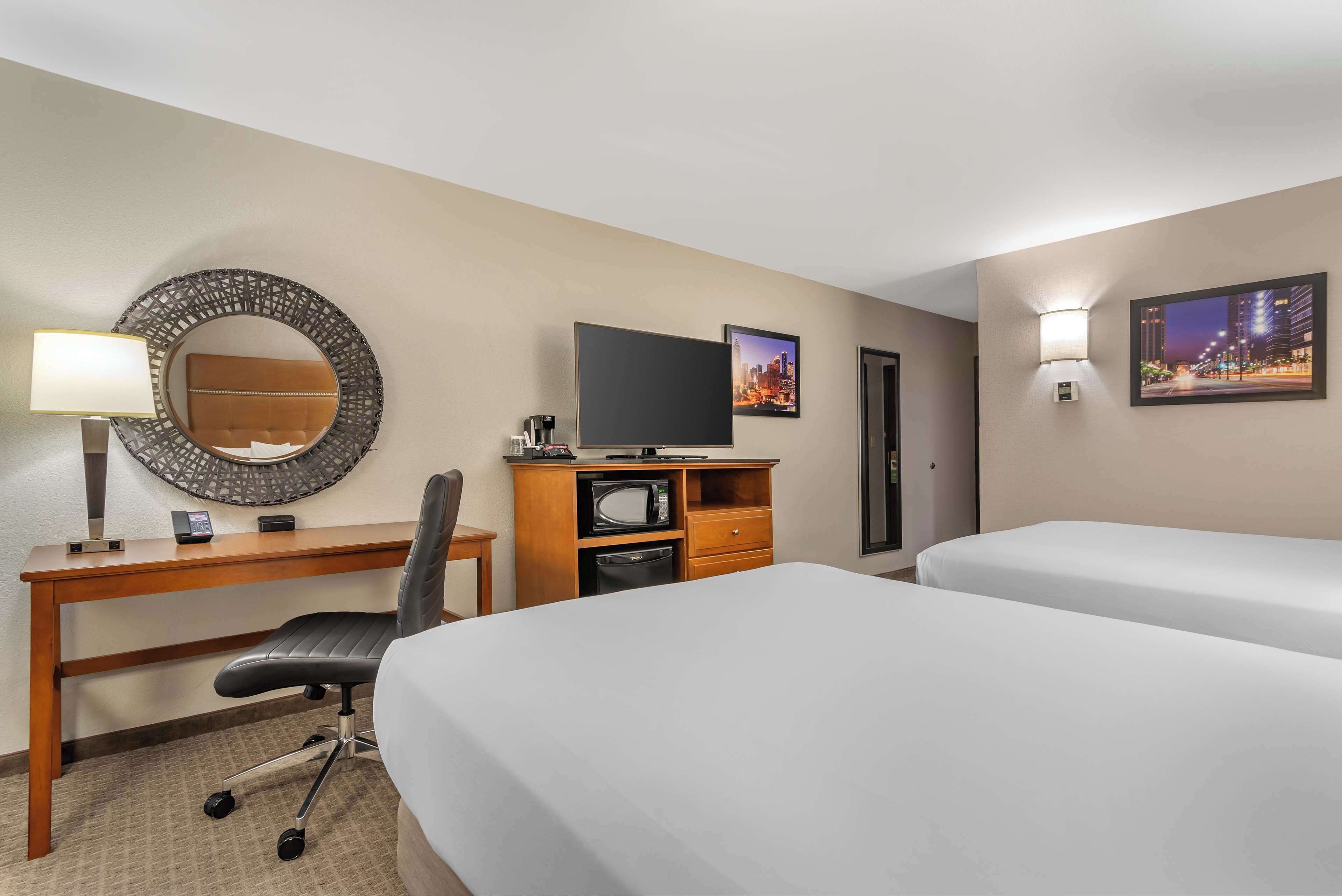 A hotel room with a desk, chair, two beds, a TV, a microwave, and a small cabinet.
