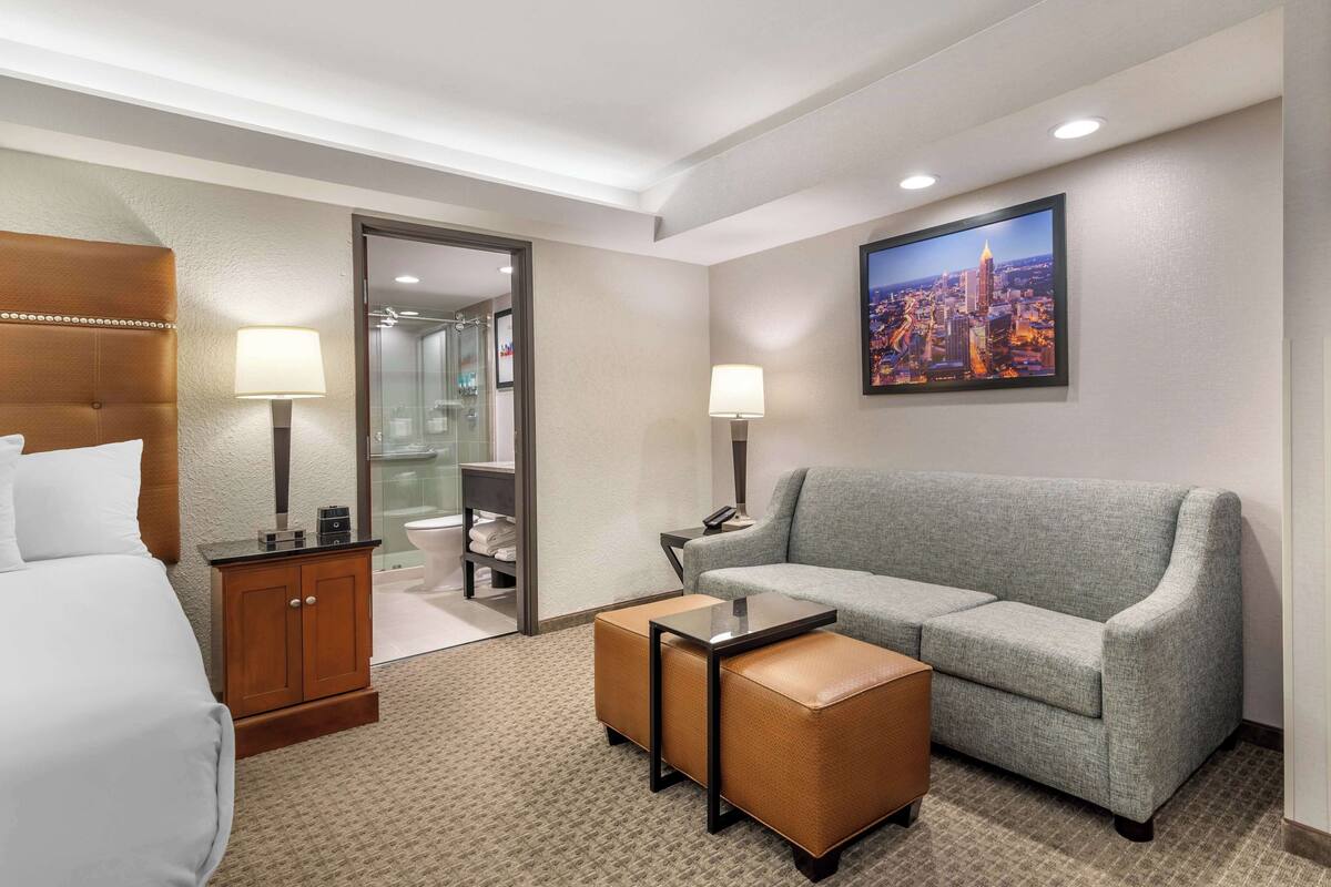 A hotel room with a bed, a grey sofa, a small table, and a cabinet.