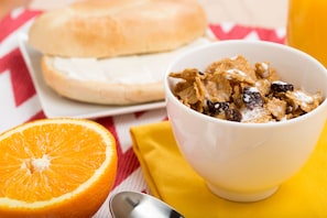 A bowl of cereal with raisins and milk, a half orange, and a sandwich on a tablecloth. - Drury Inn & Suites Atlanta Airport (Atlanta)