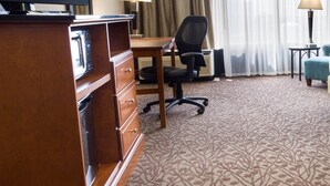 A hotel room with a flat-screen TV, a wooden dresser, a desk with a chair, a lamp, and a large window with curtains. - Drury Inn & Suites Atlanta Airport (Atlanta)