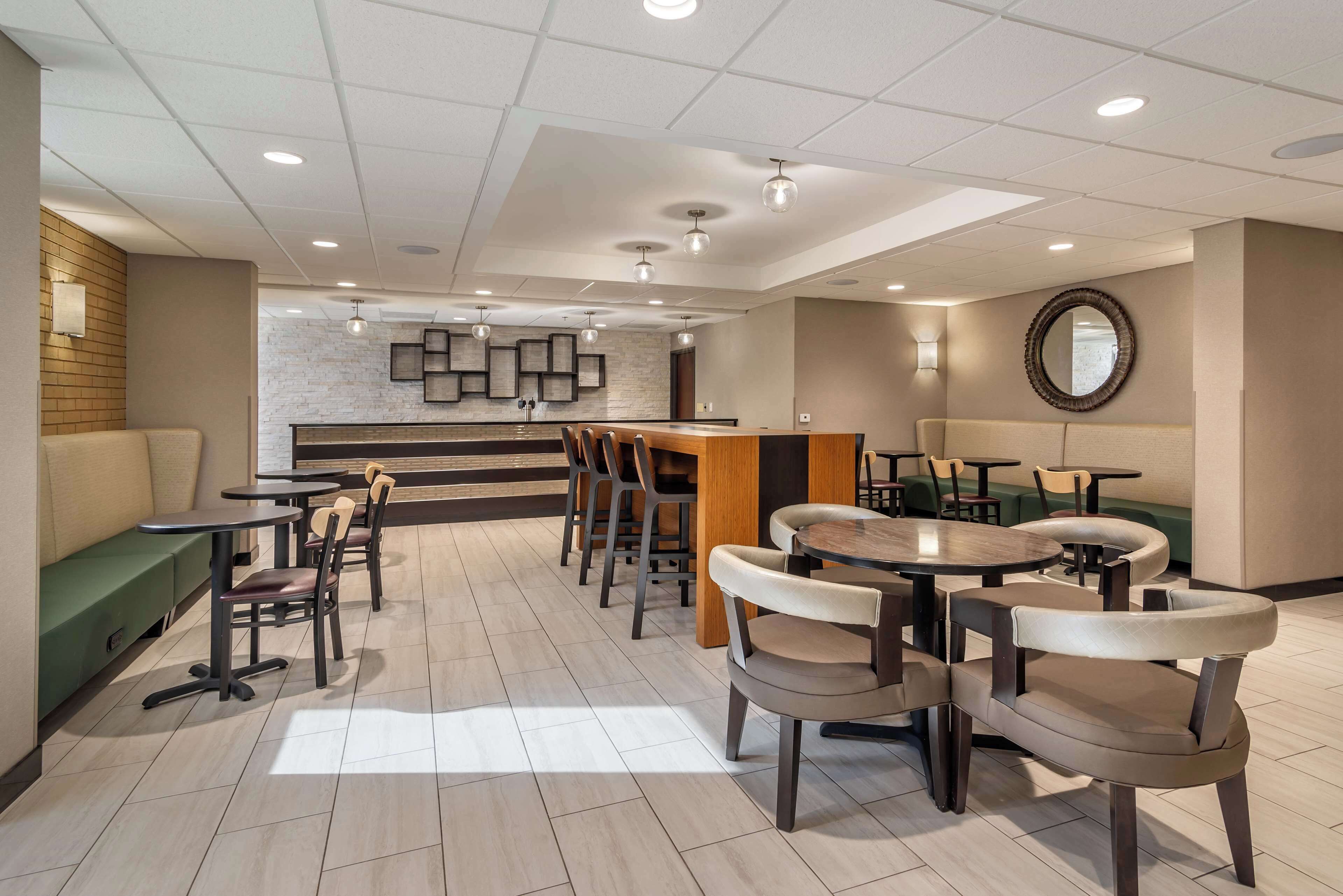 A modern hotel lobby with a reception desk, seating areas, and a kitchen in the background.