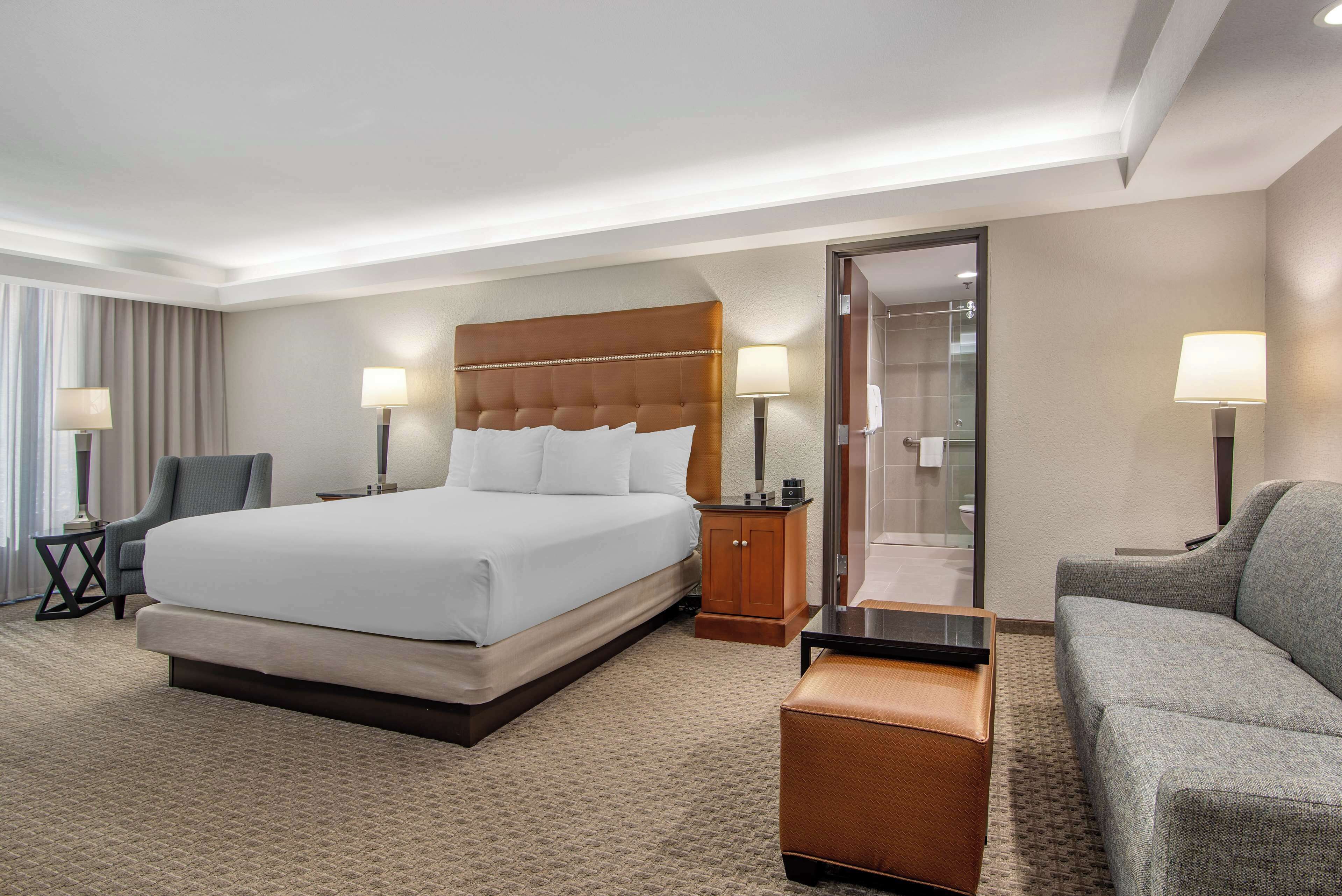 Una habitación de hotel con una cama grande, un sofá, un escritorio y un baño con ducha de vidrio.