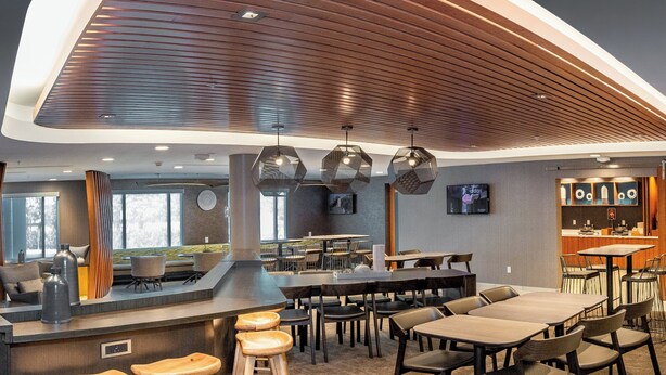 A modern restaurant with a wooden ceiling, bar stools, and a variety of seating options. - SpringHill Suites Anchorage Midtown (Anchorage)