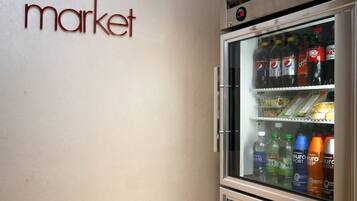 A refrigerator stocked with beverages and snacks, a wall sign reading "the market", and a digital display above the refrigerator.