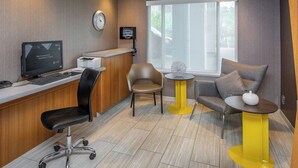 A modern office space with a desk, computer, and office chair. There is a round table with a yellow base and a white vase. A clock is visible on the wall. - SpringHill Suites Anchorage Midtown (Anchorage)