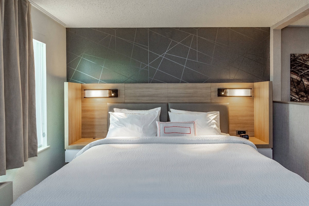 Ett modernt hotellrum med en stor säng, två sängbord och en sänggavel med ett geometriskt mönster.