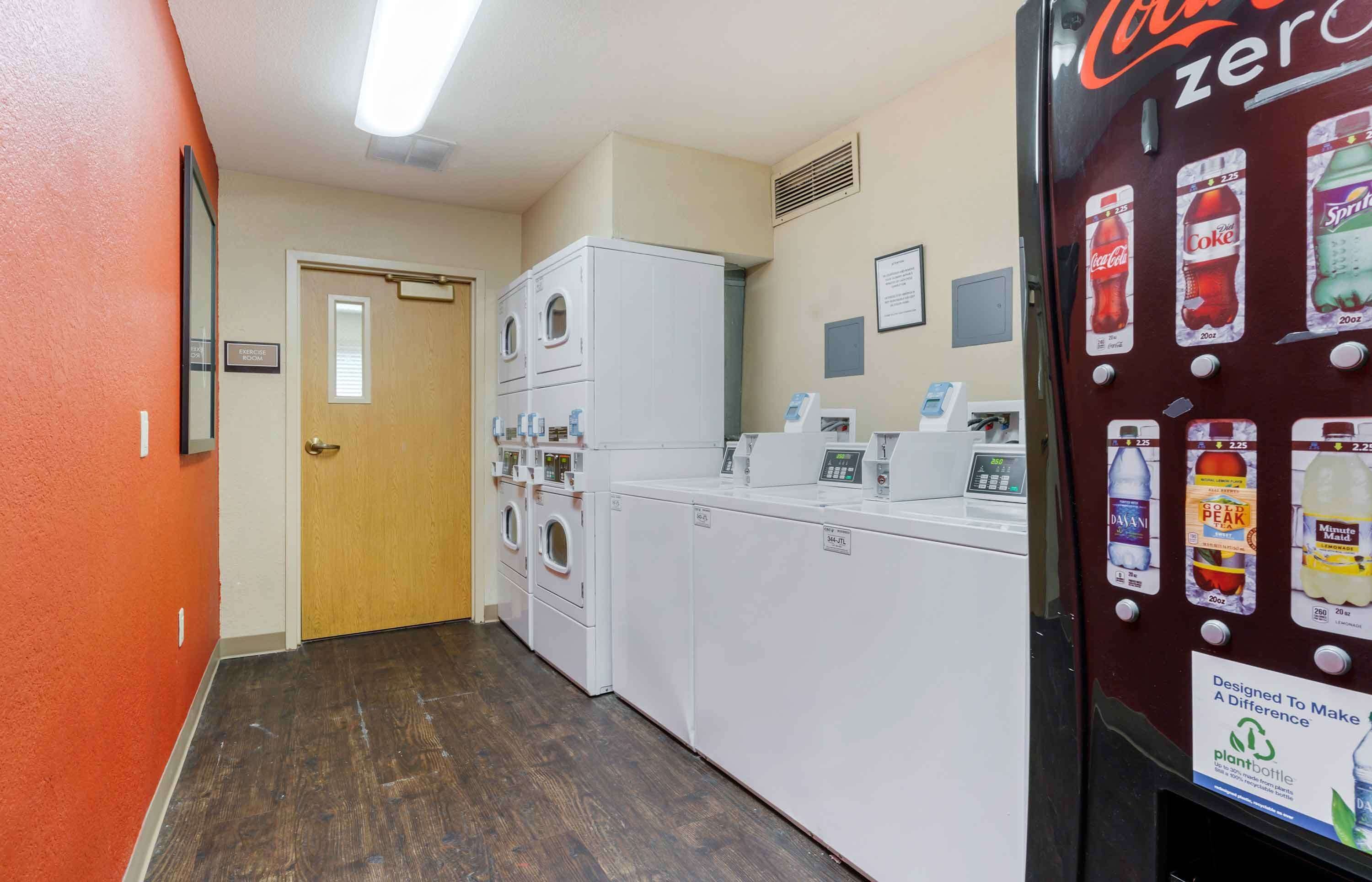 A laundry area with multiple washing machines, a dryer, and a vending machine offering beverages.