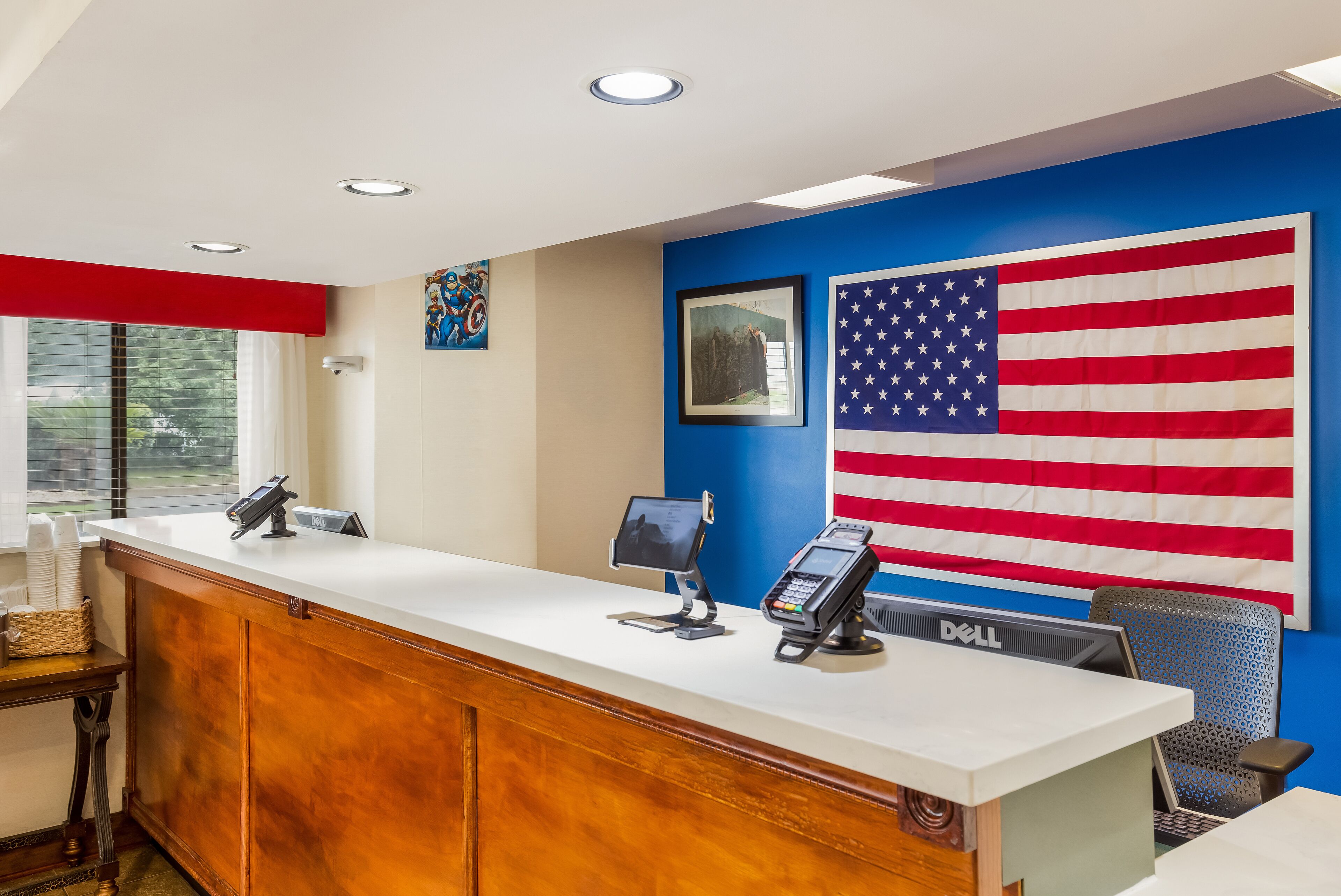 A reception desk with a computer, a phone, and a monitor. There is a large American flag on the wall and a window with blinds.