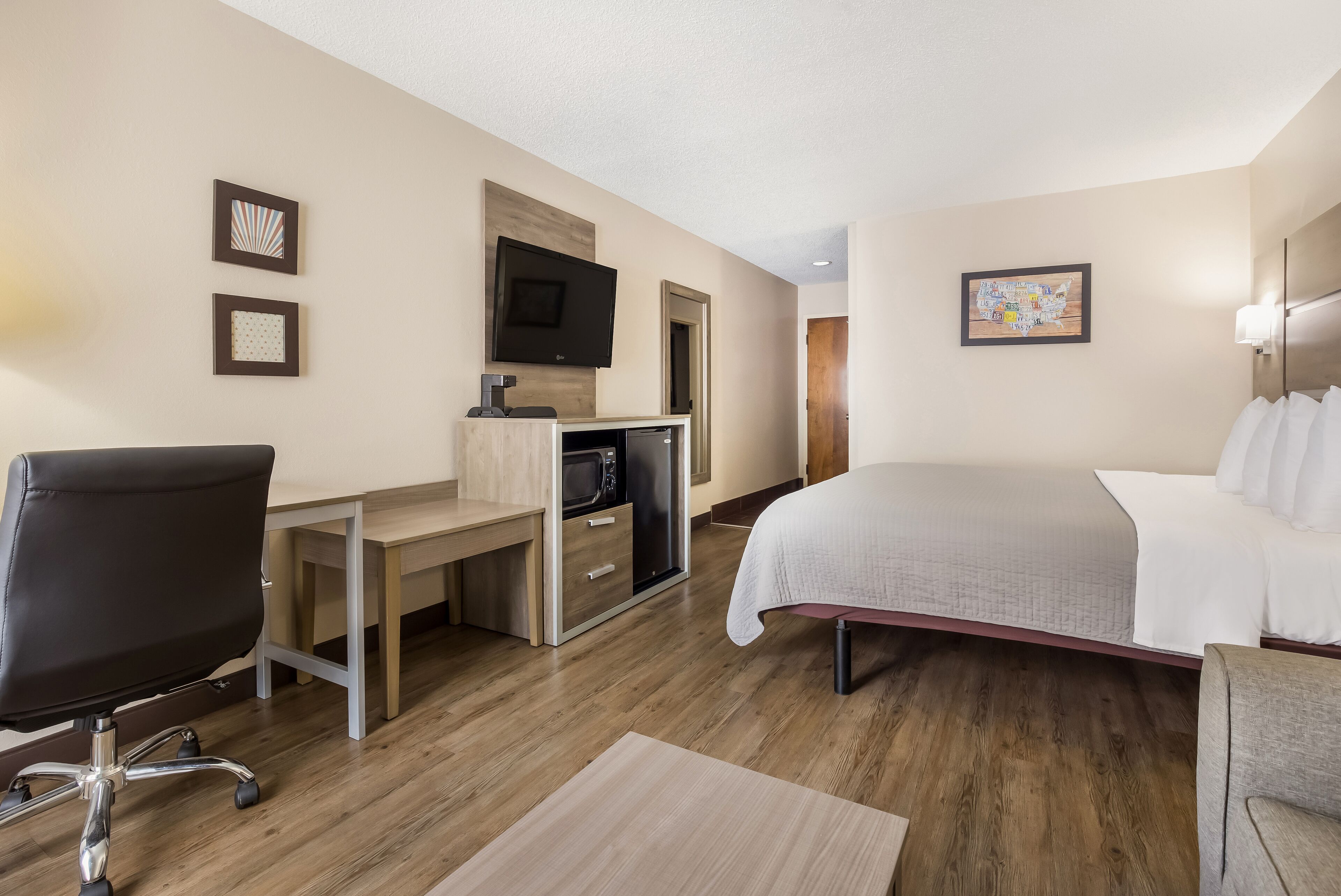 A hotel room with a bed, desk, chair, TV, and microwave.