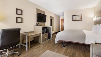 A hotel room with a bed, desk, chair, TV, and microwave.