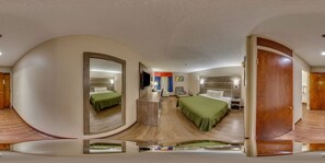 A modern hotel room with a curved mirror, a bed with green bedding, a wooden floor, and a wooden door.