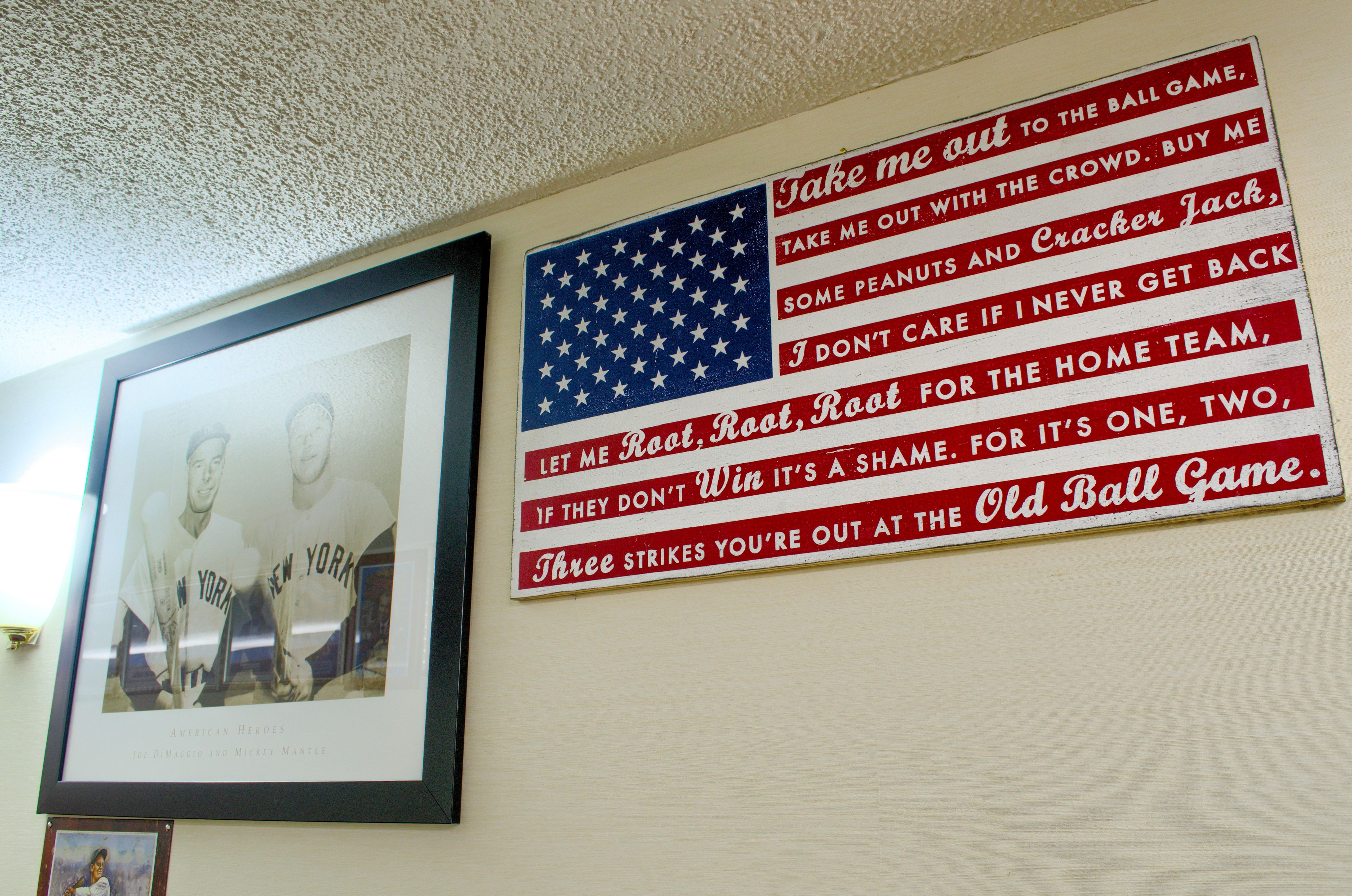 A framed quote on a wall with an American flag and a framed photograph of two baseball players.
