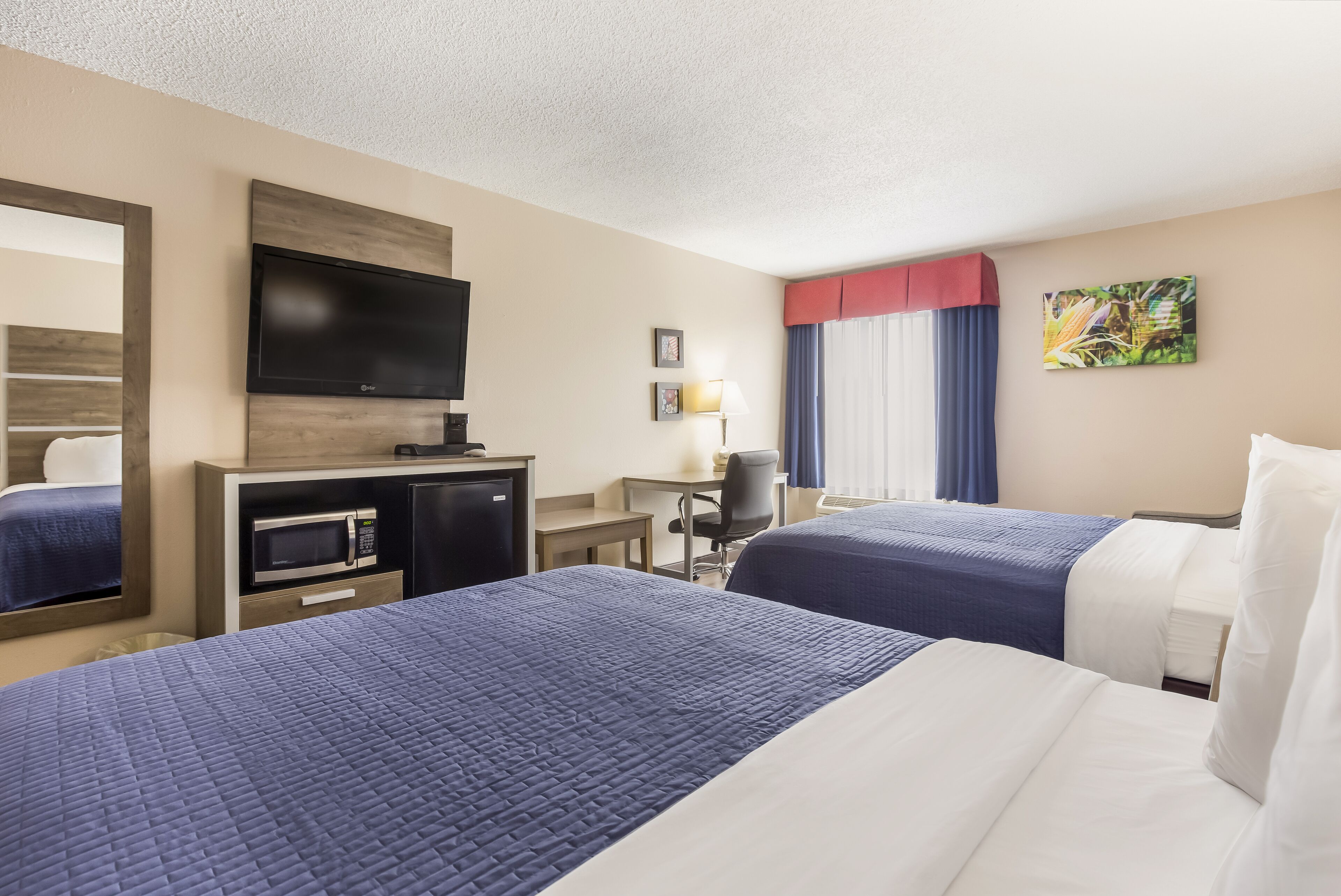 A hotel room with two beds, a desk, a microwave, a TV, and a window with curtains.