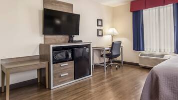 Habitación de hotel con escritorio, televisor, microondas, cama y ventana con cortinas.