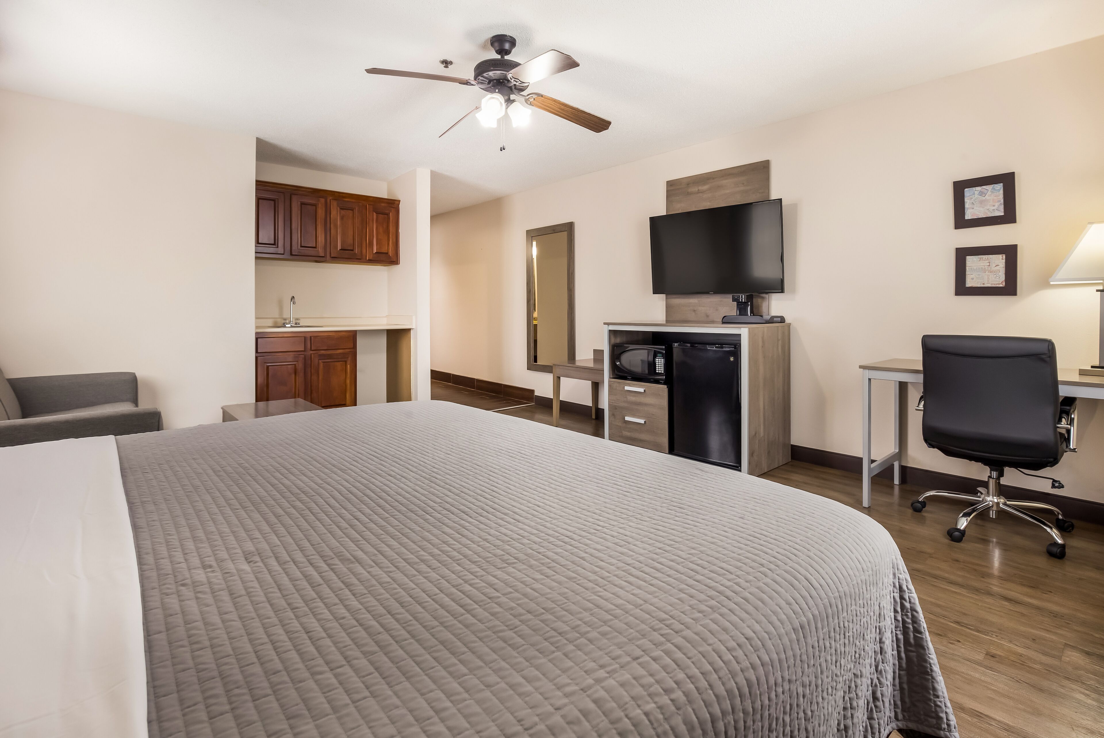 A hotel room with a bed, a desk, a chair, a television, and a kitchenette.