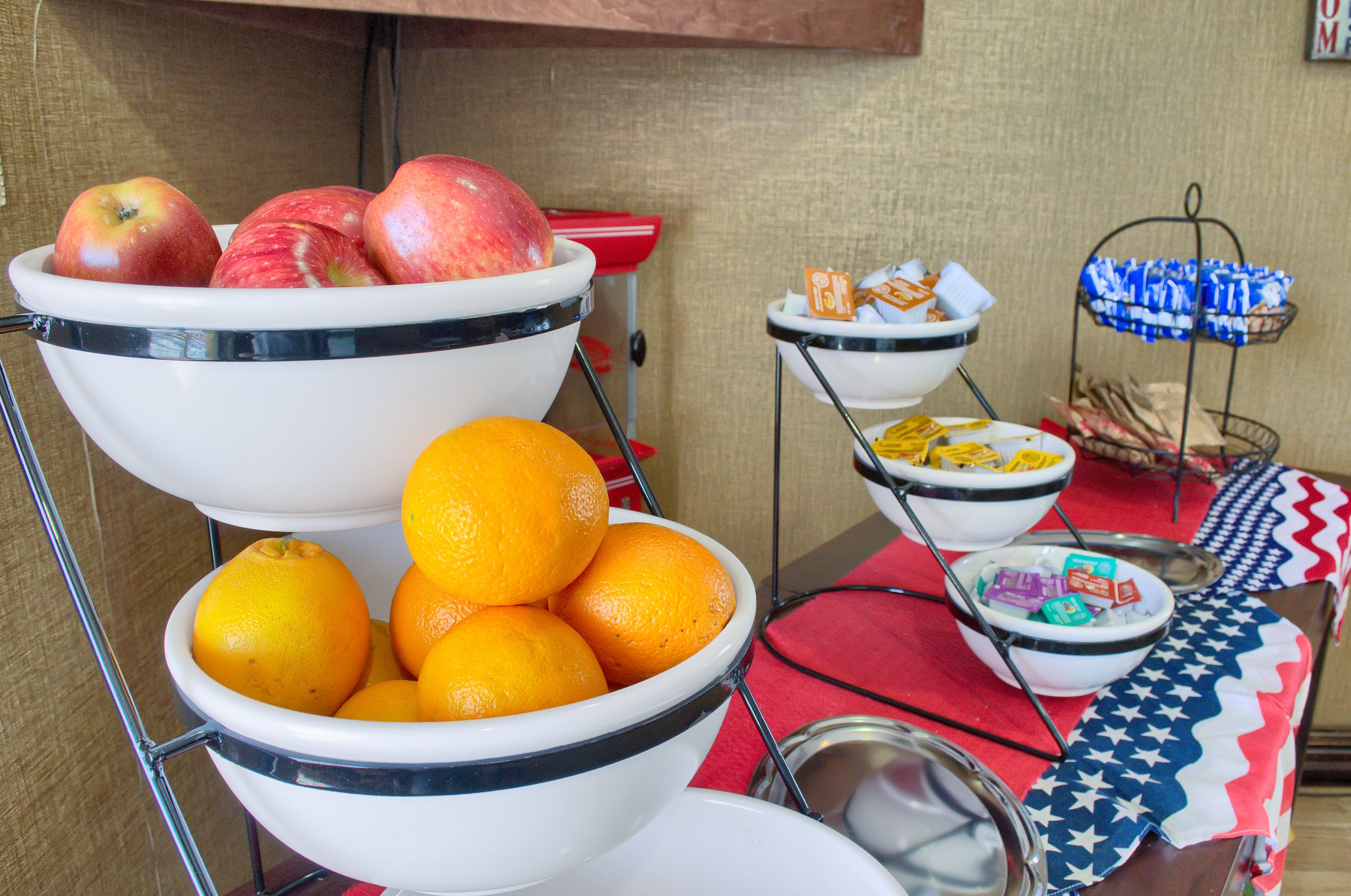A buffet setup with bowls of apples and oranges, and a tray with snacks.