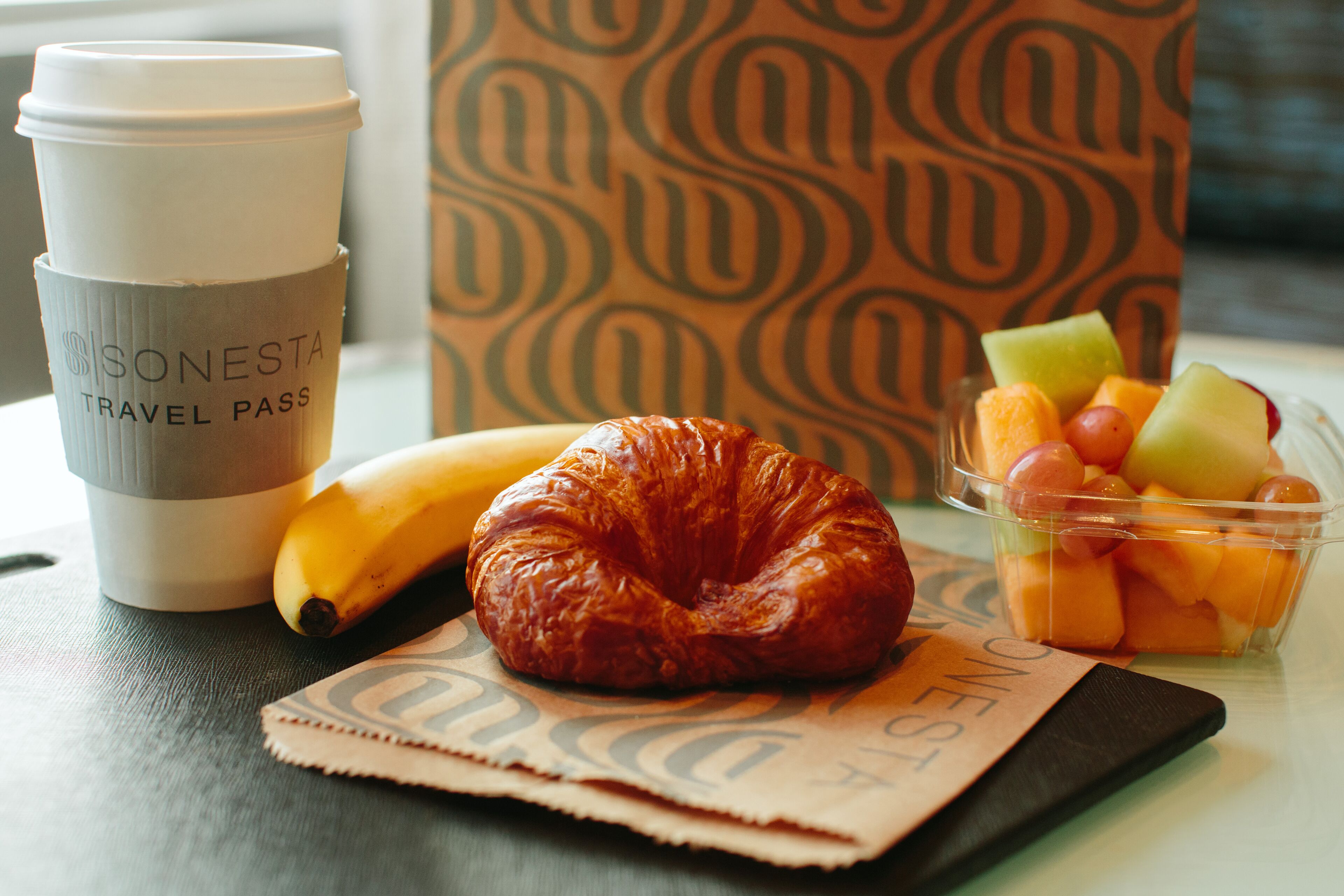 Un abonnement de transport, un croissant, une banane et une barquette de fruits sur une table.
