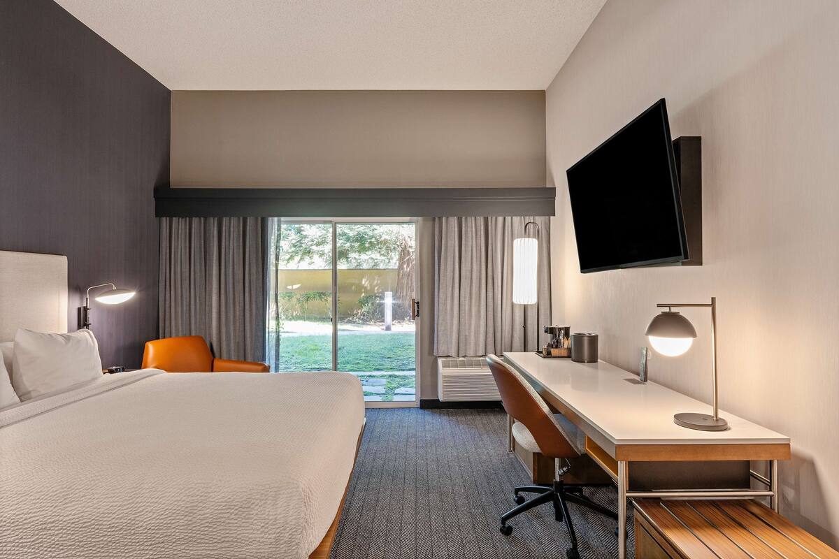 A hotel room with a bed, desk, chair, TV, and a view of the outdoors.